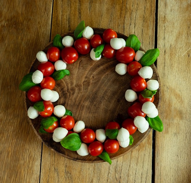 Hvite mozerella baller, røde cherrytomater og grønn basilikum ligger lagvis og i en sirkel. 