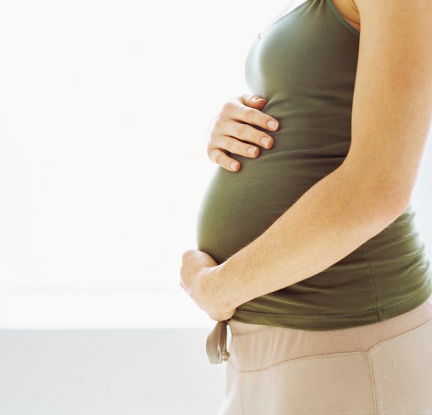 En gravidmage hvor kvinnen som er gravid klemmer på magen sin. Hun går med en beige bukse og grønn topp.