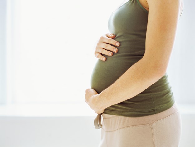 En gravidmage hvor kvinnen som er gravid klemmer på magen sin. Hun går med en beige bukse og grønn topp.